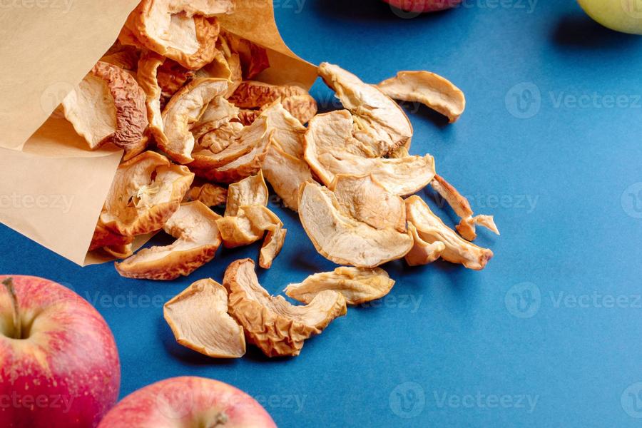 17383238-sac-en-papier-avec-des-tranches-de-pommes-sechees-dispersees-et-des-fruits-entiers-sur-fond-bleu-photo